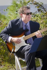 Teacher Drew Thompson playing guitar by the beach